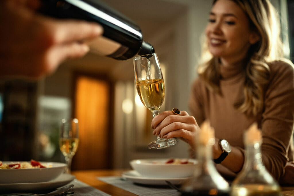 Close-up of unrecognizable man serving Champagne to his girlfriend while having dinner at dining table.